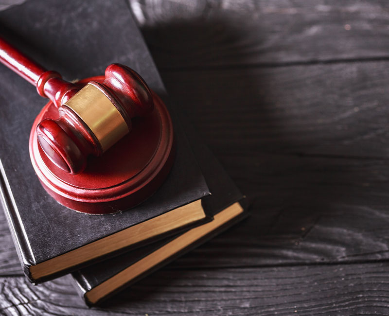 A wooden judge’s gavel rests on top of two black books with gold-edged pages, placed on a dark wooden surface.